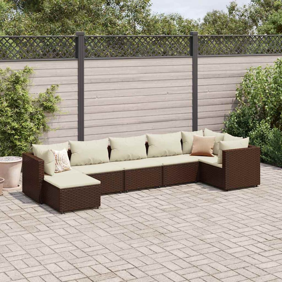 Divano componibile da esterno con cuscini beige e struttura in vimini marrone. Patio con piante.