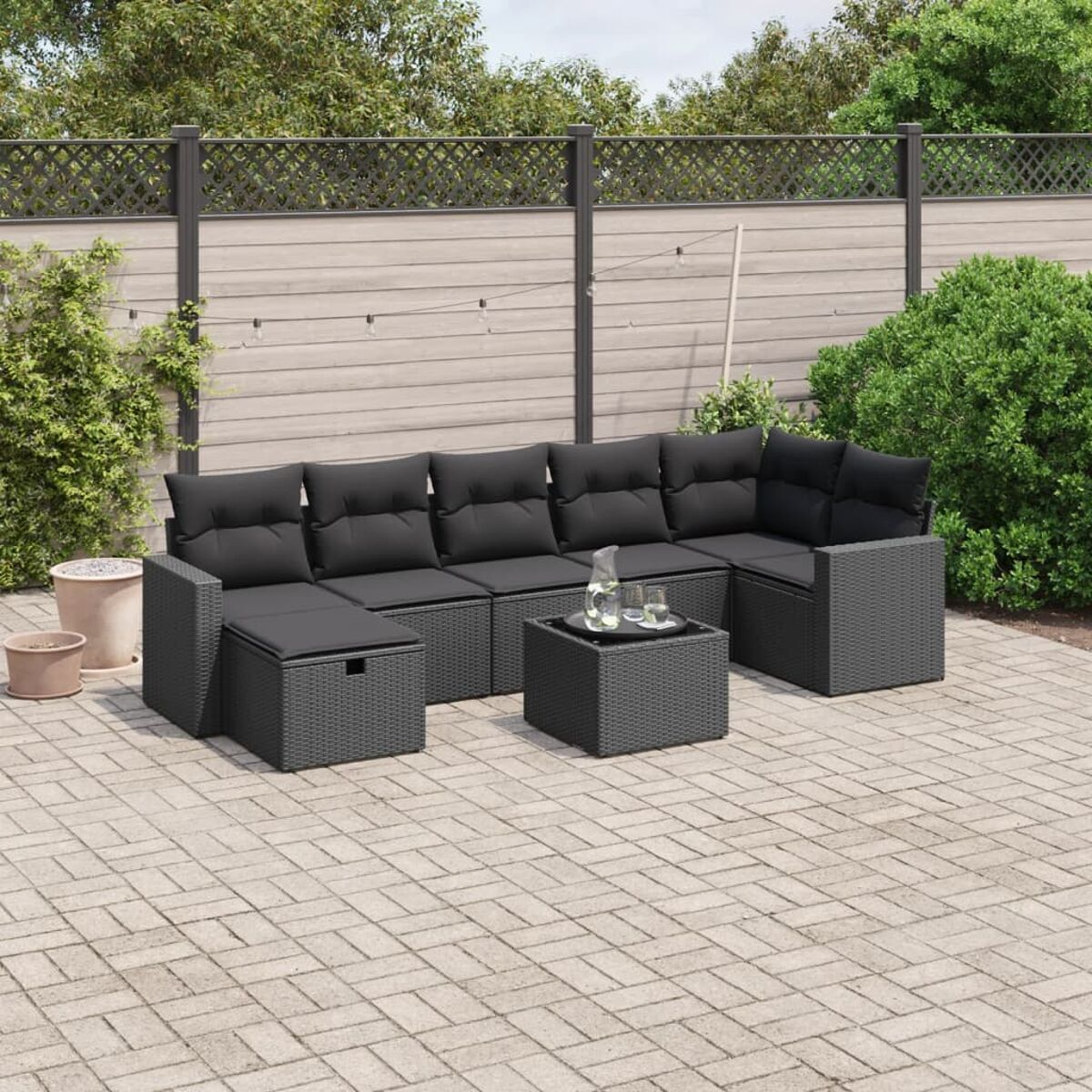 Graues Rattan-Sofa-Set im Freien mit schwarzen Kissen, einem Couchtisch und einer Ziegelterrasse.