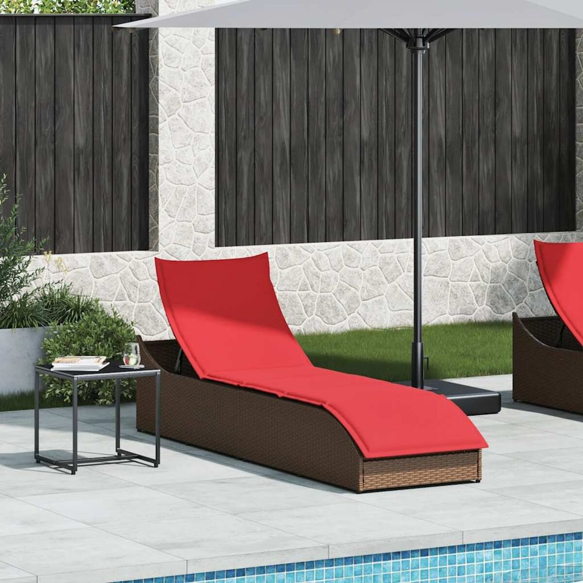 Lettino prendisole imbottito rosso su un patio. Un tavolino e un ombrellone sono nelle vicinanze. Muro di pietra sullo sfondo.