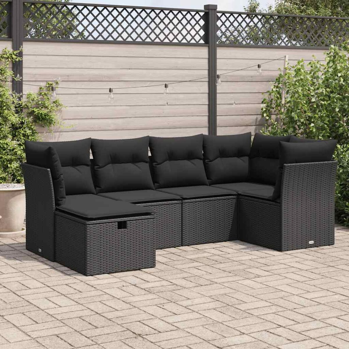 Ein schwarzes Outdoor-Ecksofa auf einer Ziegelterrasse, umgeben von Pflanzen und einem Zaun.