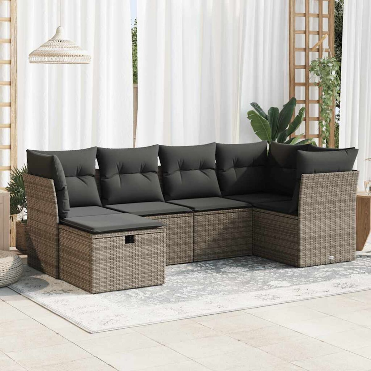 Rattan-Ecksofa mit dunkelgrauen Kissen auf einer Terrasse. Ein Teppich und ein Beistelltisch sind vorhanden.