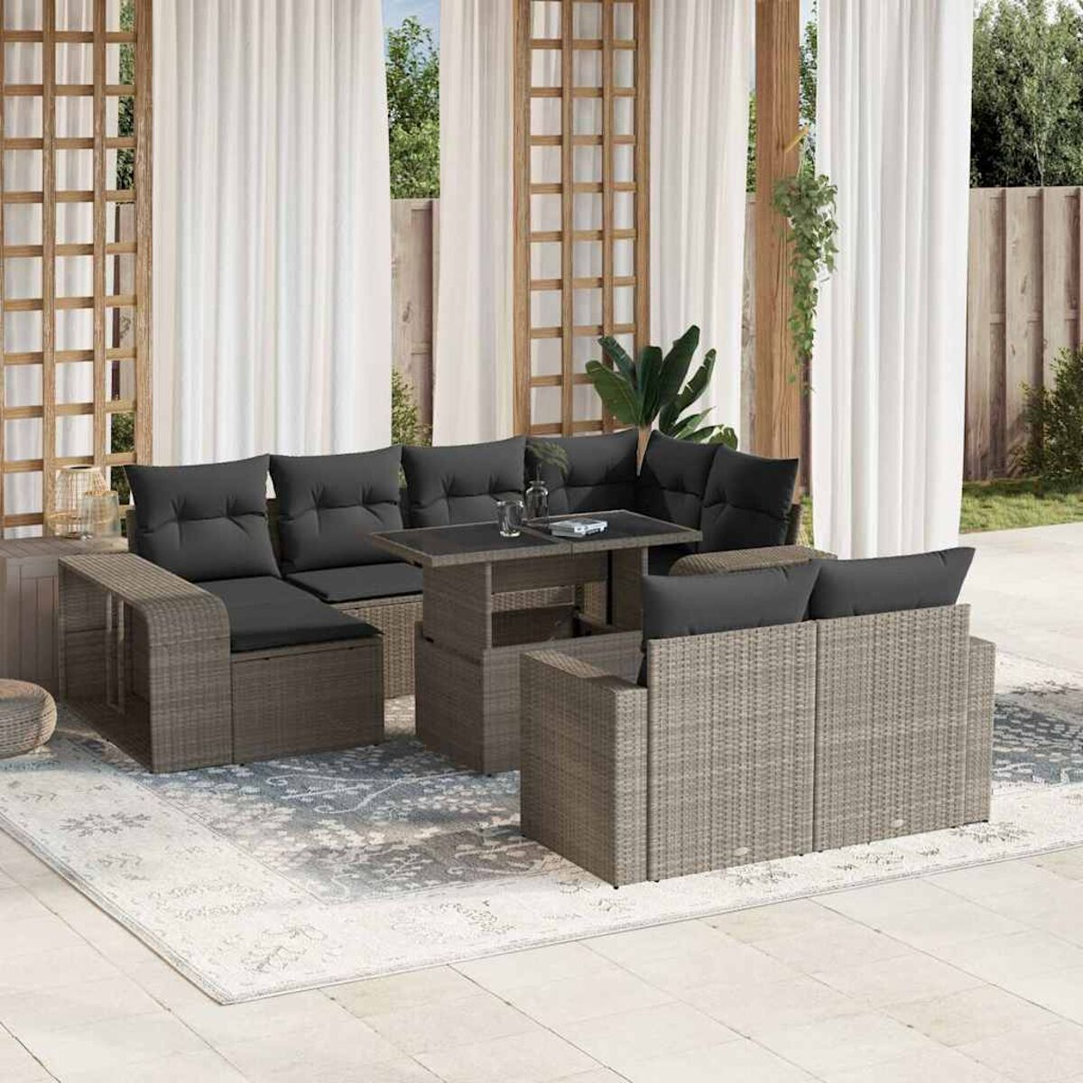 Rattansofa-Set mit Tisch, grauen Kissen. Auf einem Teppich auf einer Terrasse, mit Vorhängen.