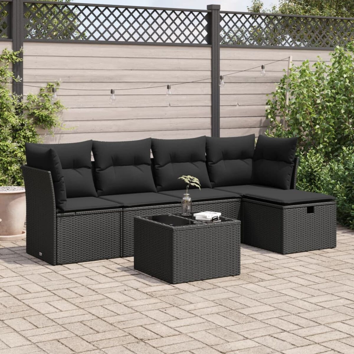 Schwarzes Outdoor-Ecksofa mit einem Couchtisch. Die Szene spielt auf einer Terrasse mit Lichterketten.