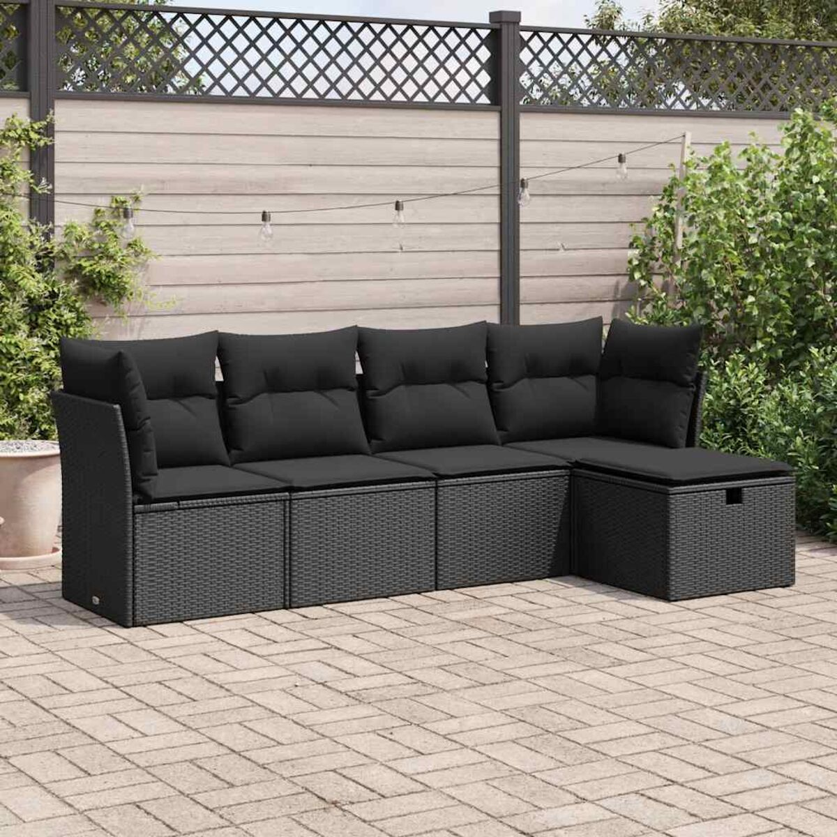 Divano angolare in rattan nero su un patio. Include cuscini e un pouf contenitore.