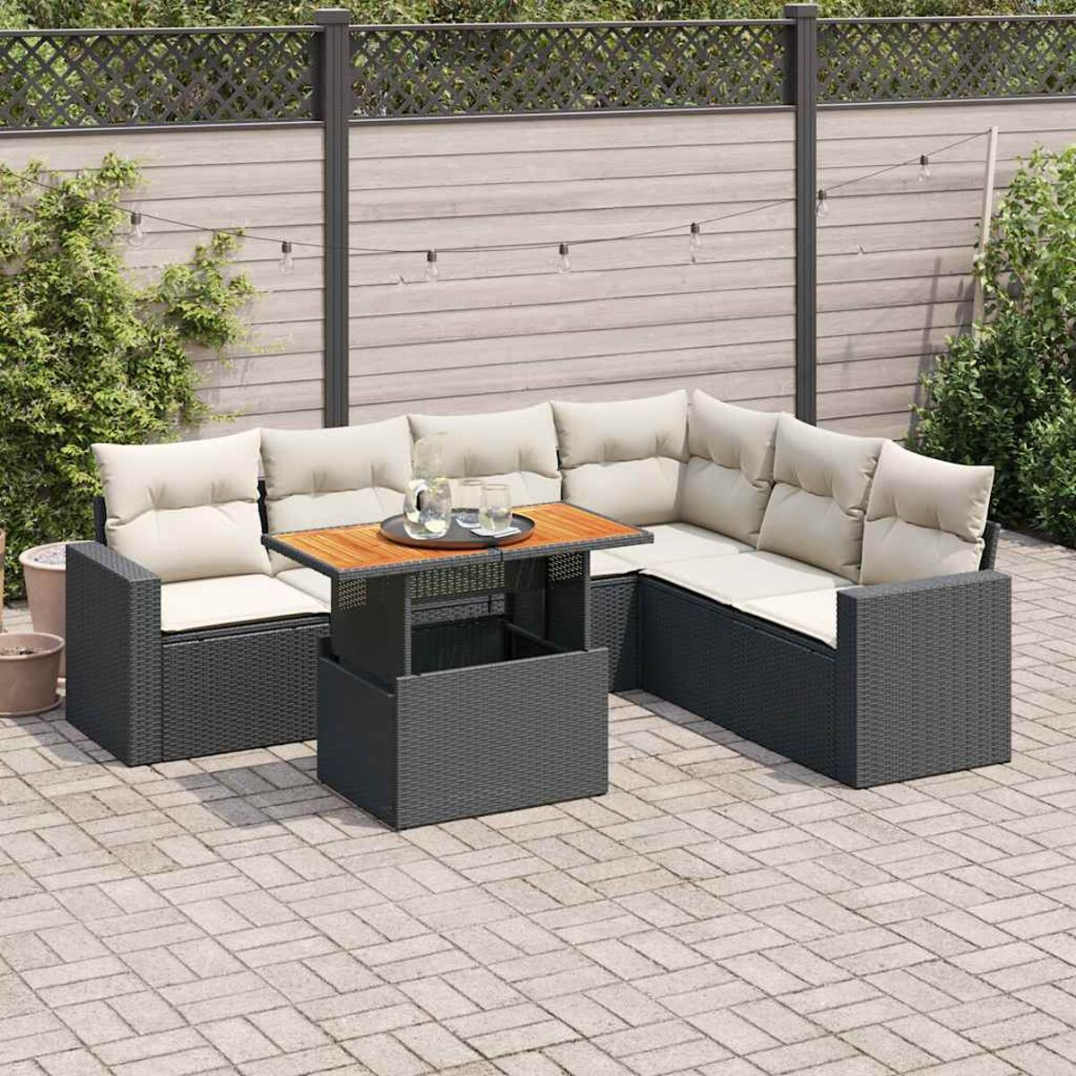 Divano componibile da esterno con cuscini beige e un tavolo in legno. Su un patio pavimentato con recinzione.