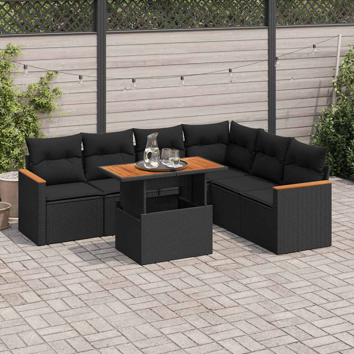 Divano angolare da esterno in vimini nero con cuscini neri. Tavolo con piano sollevabile. Patio in mattoni.