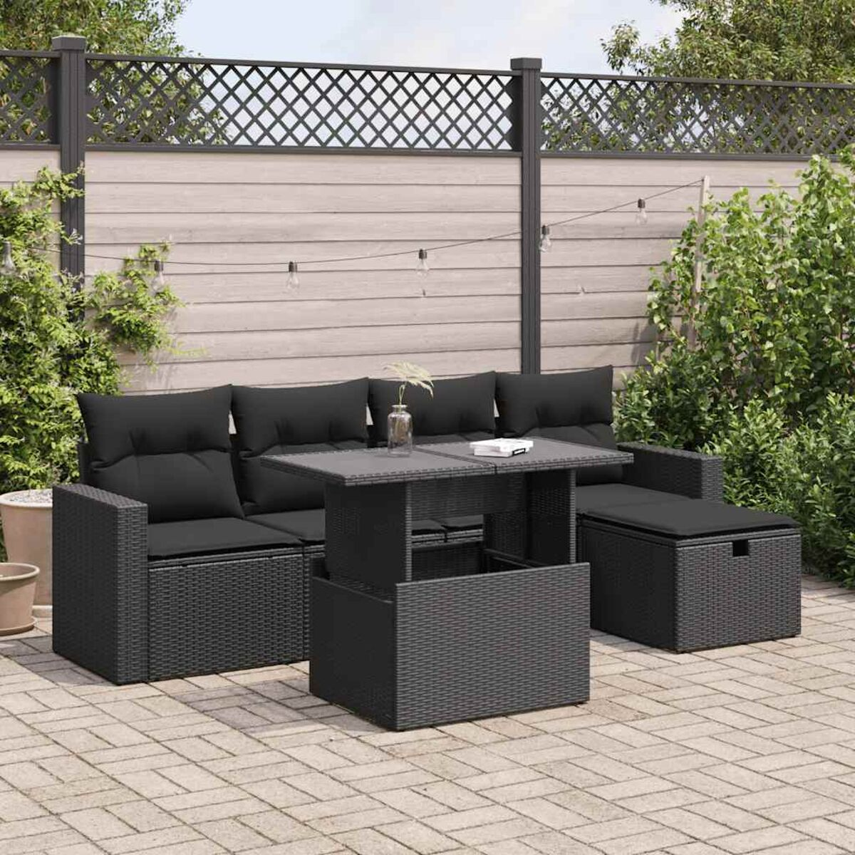 Ein Outdoor-Terrassenset mit einem schwarzen Sofa im Korbstil, Tisch und Ottomane auf gepflasterter Oberfläche.