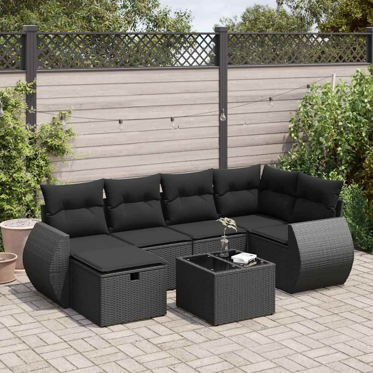 Ein schwarzes Outdoor-Sofaset. Enthält ein Ecksofa, einen Couchtisch und eine Aufbewahrungshocker. Grün im Hintergrund.
