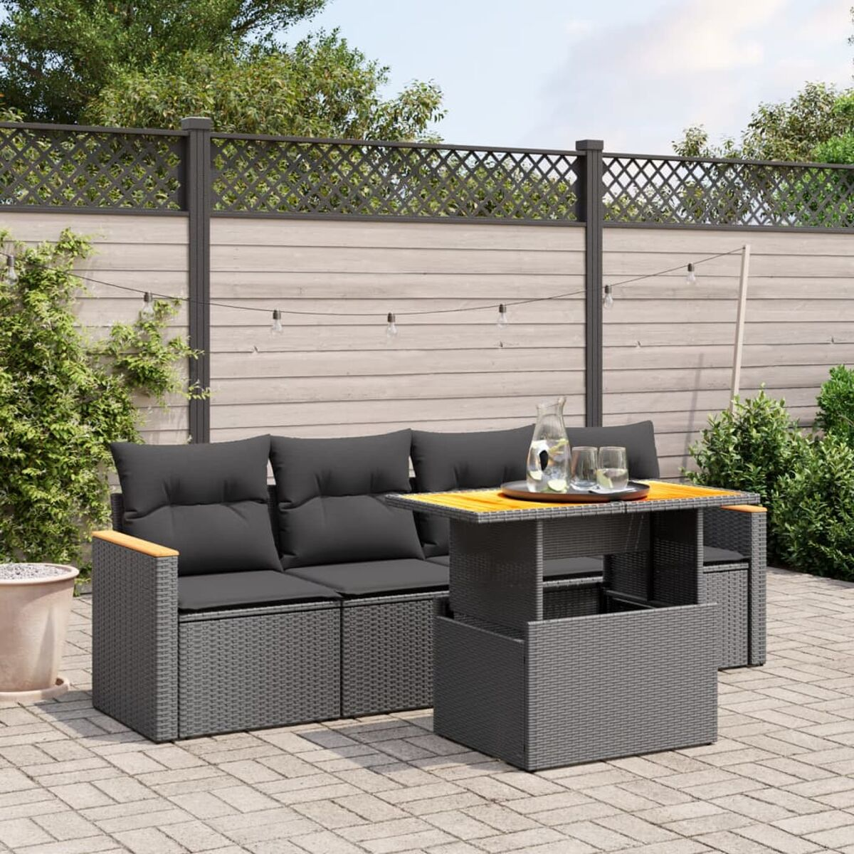 Graues Ecksofa aus Korbgeflecht für den Außenbereich mit grauen Kissen. Tisch mit Hubtisch. Ziegelterrasse.