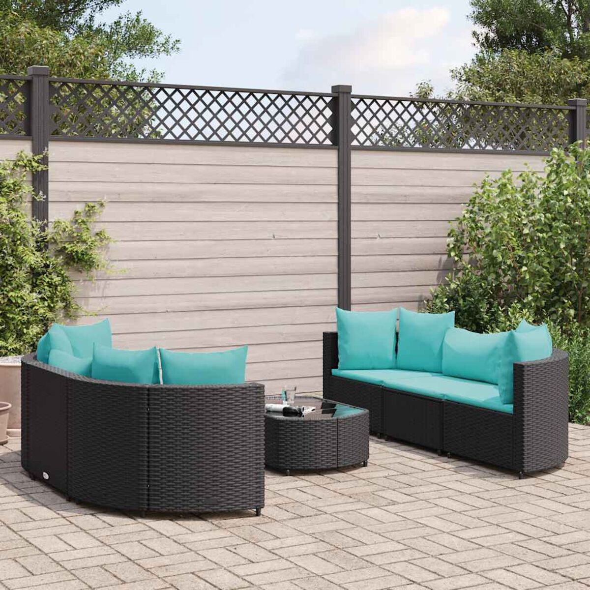 Schwarzes Rattan-Gartenmöbel-Set mit türkisfarbenen Kissen, auf einer gepflasterten Terrasse mit Spalier im Hintergrund.