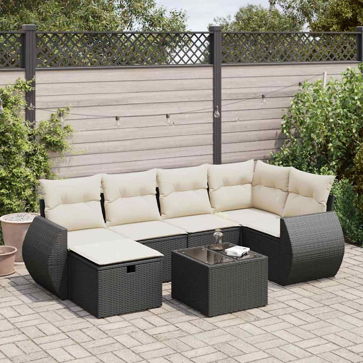 Schwarzes Outdoor-Ecksofa aus Korbgeflecht mit cremefarbenen Kissen. Ein Glastisch steht in der Mitte.