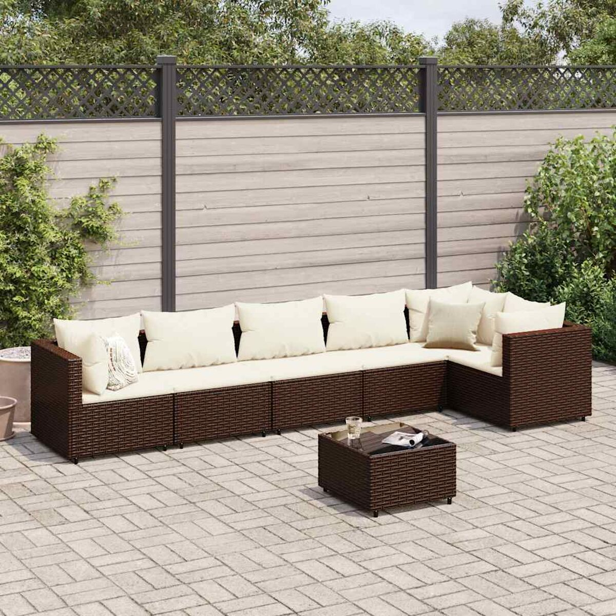 Terrassenset mit dunkelbraunem Ecksofa aus Korbgeflecht und quadratischem Couchtisch. Weiße Kissen.