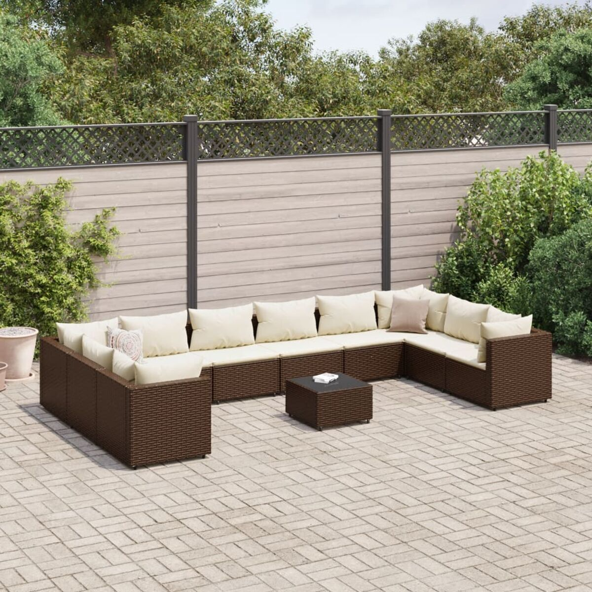 Juego de patio al aire libre. Sofá de ratán marrón, cojines beige. Fondo oscuro, patio de ladrillo. Elementos decorativos.
