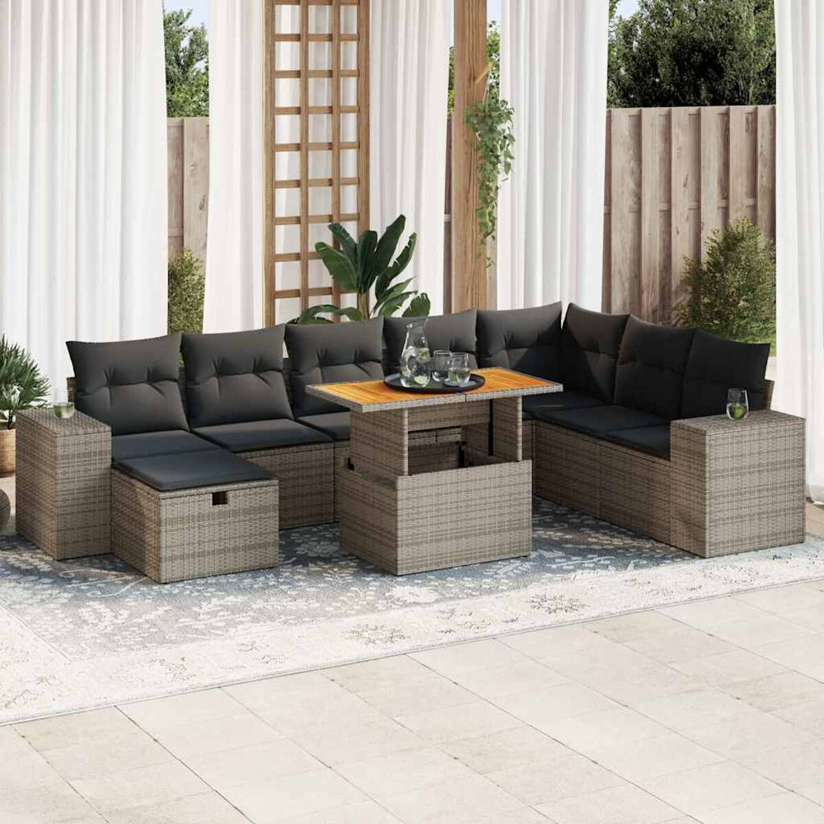 Un juego de muebles de exterior de ratán gris, cojines negros, una mesa de madera con bebidas. La escena es al aire libre.