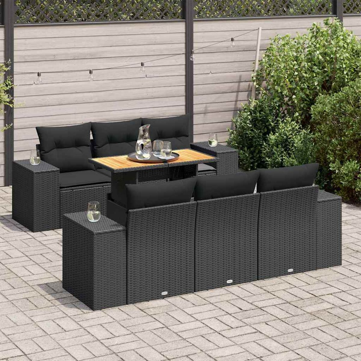 Set divano da esterno in rattan con tavolo e tavolini. Cuscini neri visibili.