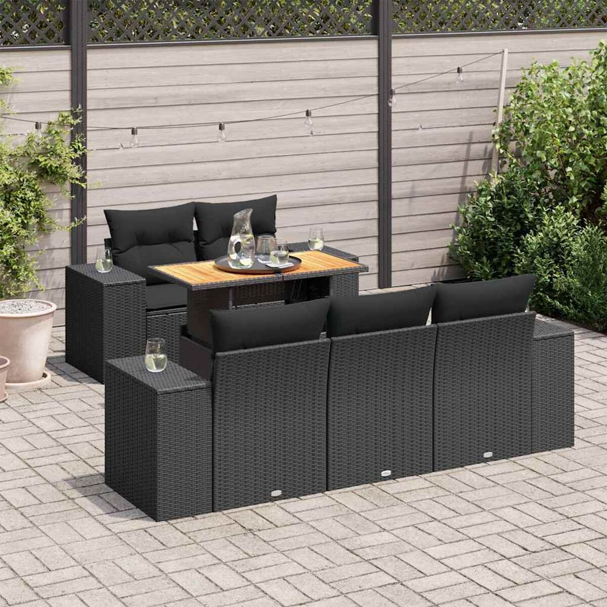 Set da patio con divano componibile in vimini nero, tavolino quadrato, cuscini neri e tavolini laterali.