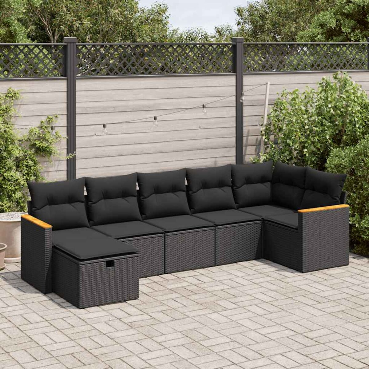 Divano componibile da esterno grigio scuro con cuscini neri, su un patio con sfondo di recinzione in legno.