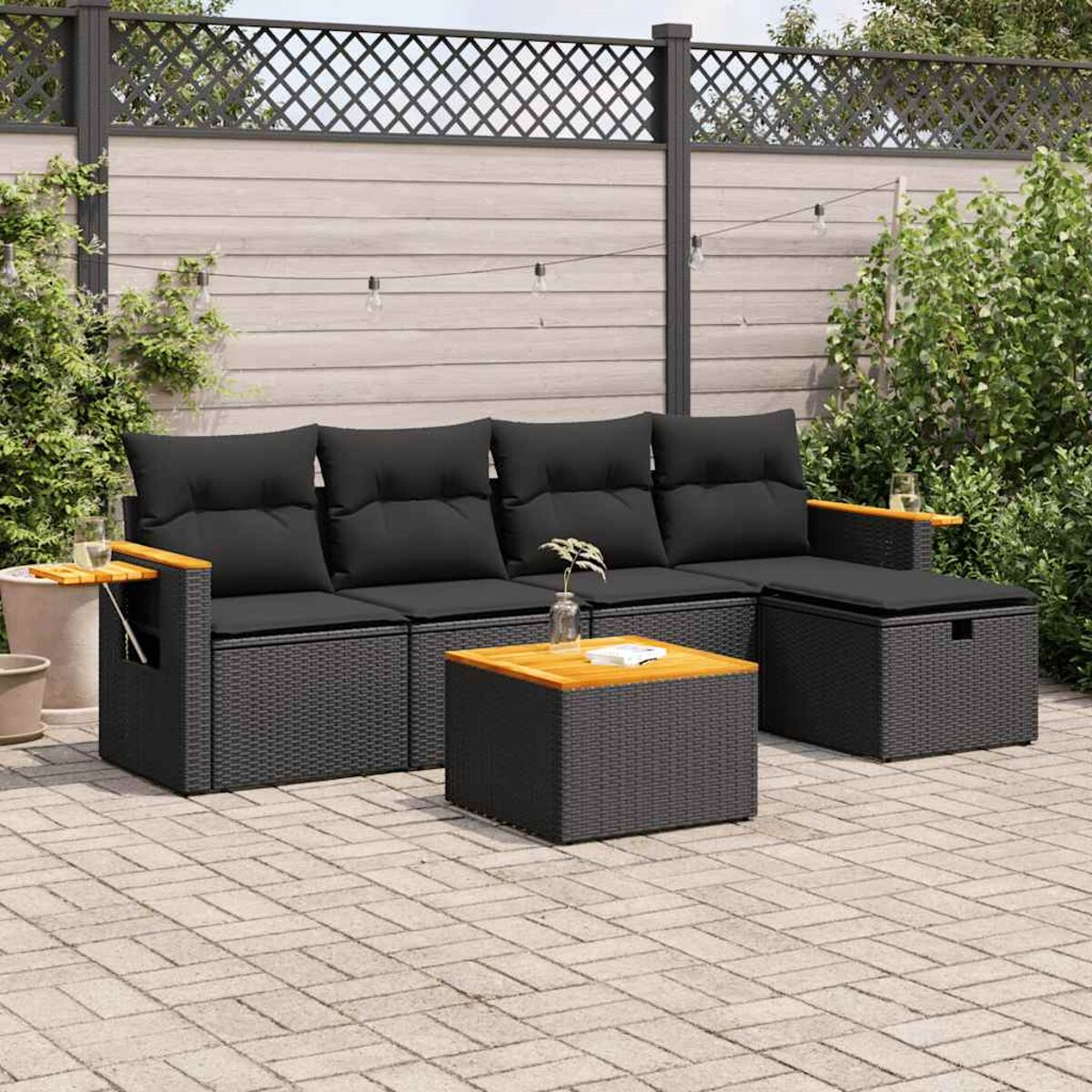 Gartenmöbel-Set mit schwarzen Kissen auf einer Terrasse. Beinhaltet ein Sofa, einen Tisch und eine Aufbewahrungsottomane.
