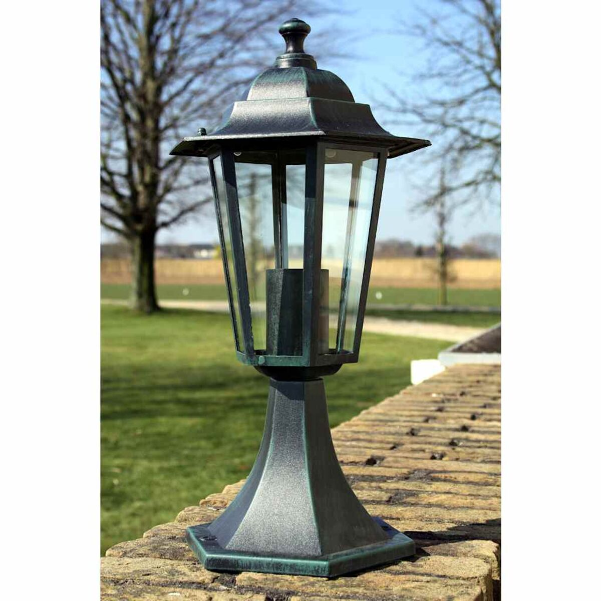 Schwarze Außenlampe auf einer Backsteinmauer, Grün im Hintergrund.