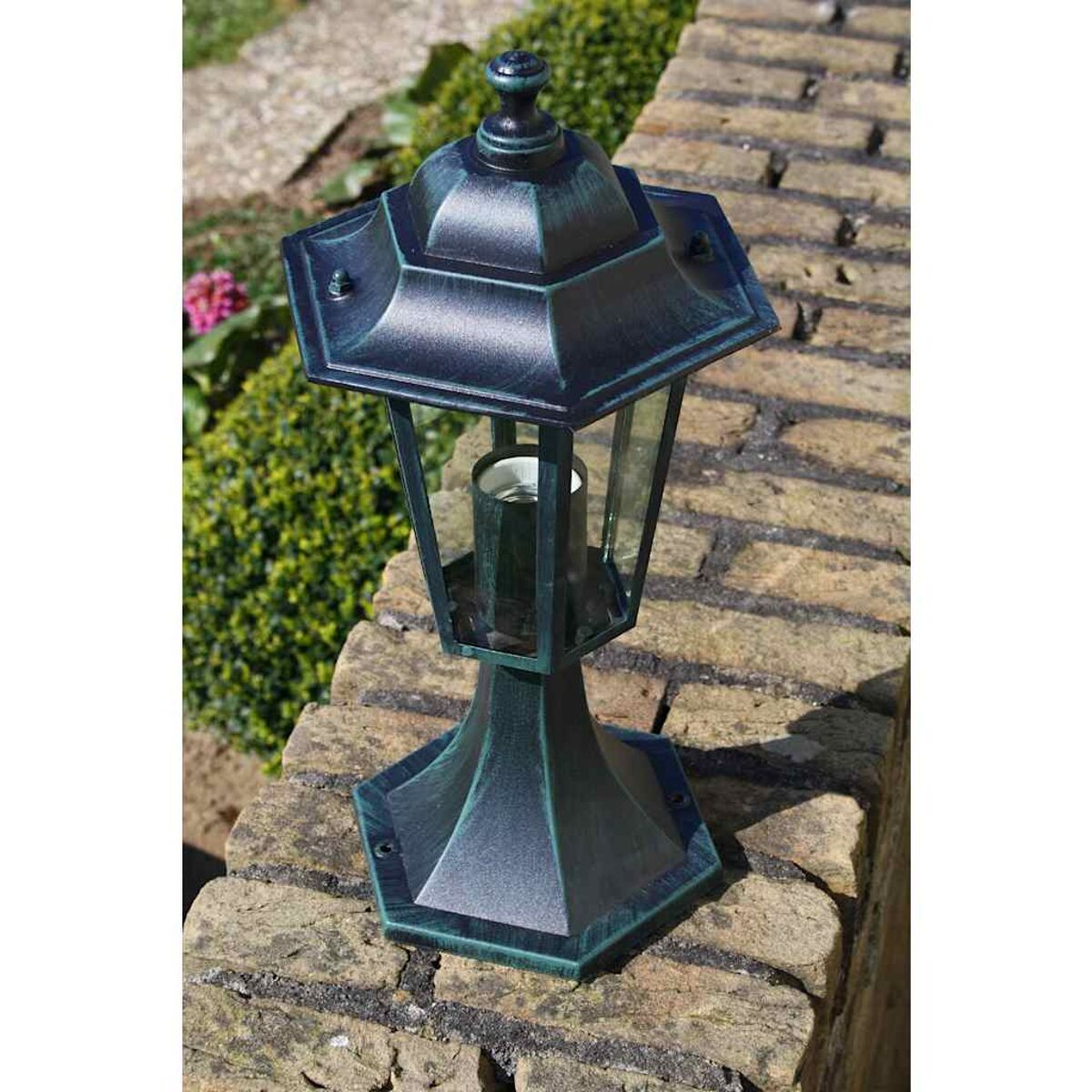 Außenlampe an Ziegelmauer. Grün und Bronze. Ein Busch und grüne Pflanzen dahinter.