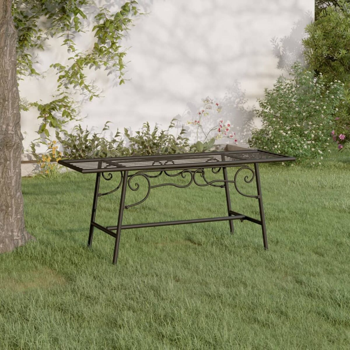 Ein langer, verzierter Metalltisch steht im Freien in einem Garten mit Gras, Blumen und einer weißen Wand.