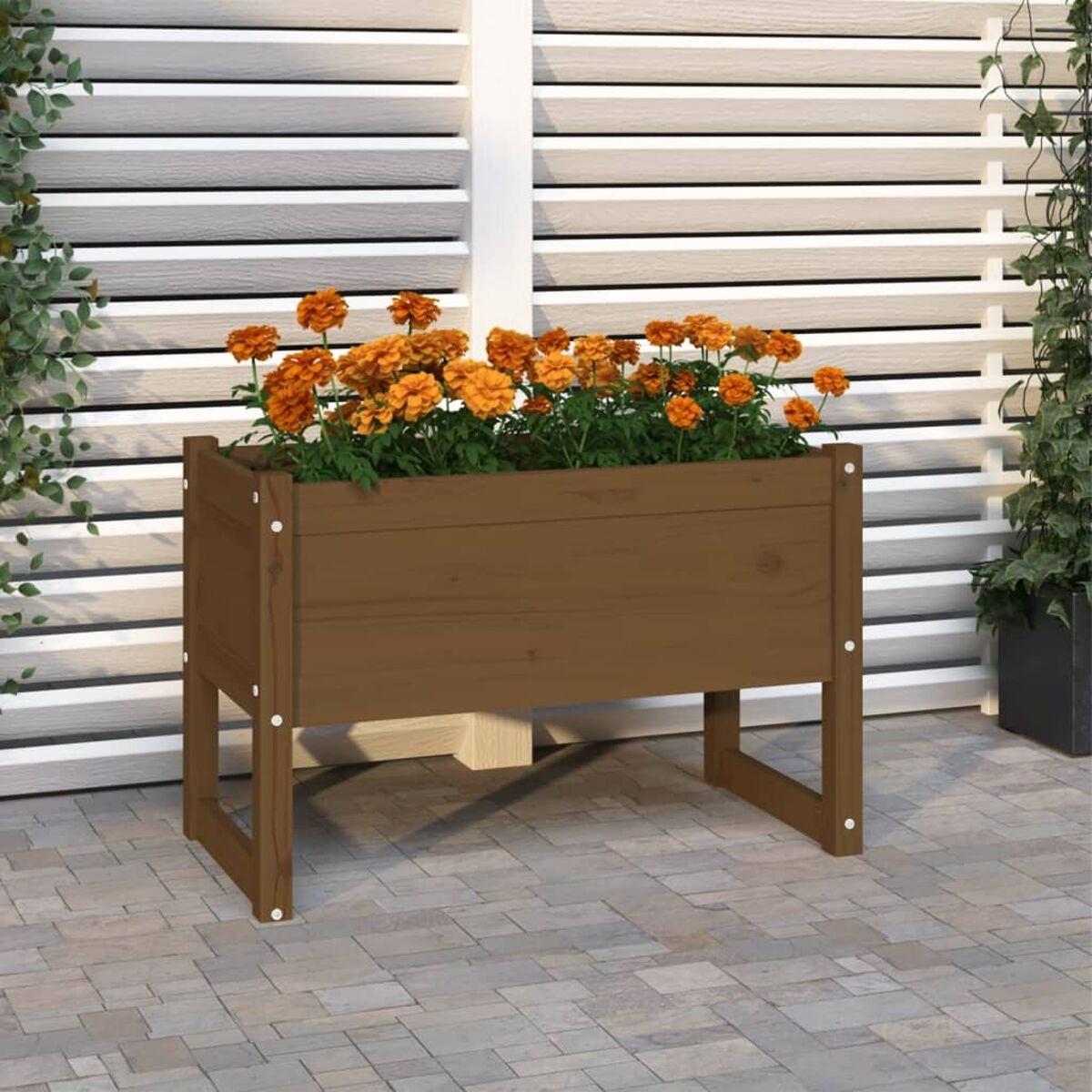 Brauner Holzpflanzer mit orangefarbenen Blumen. Steht auf einer Backsteinterrasse, Hintergrund mit weißer und grauer Wand.