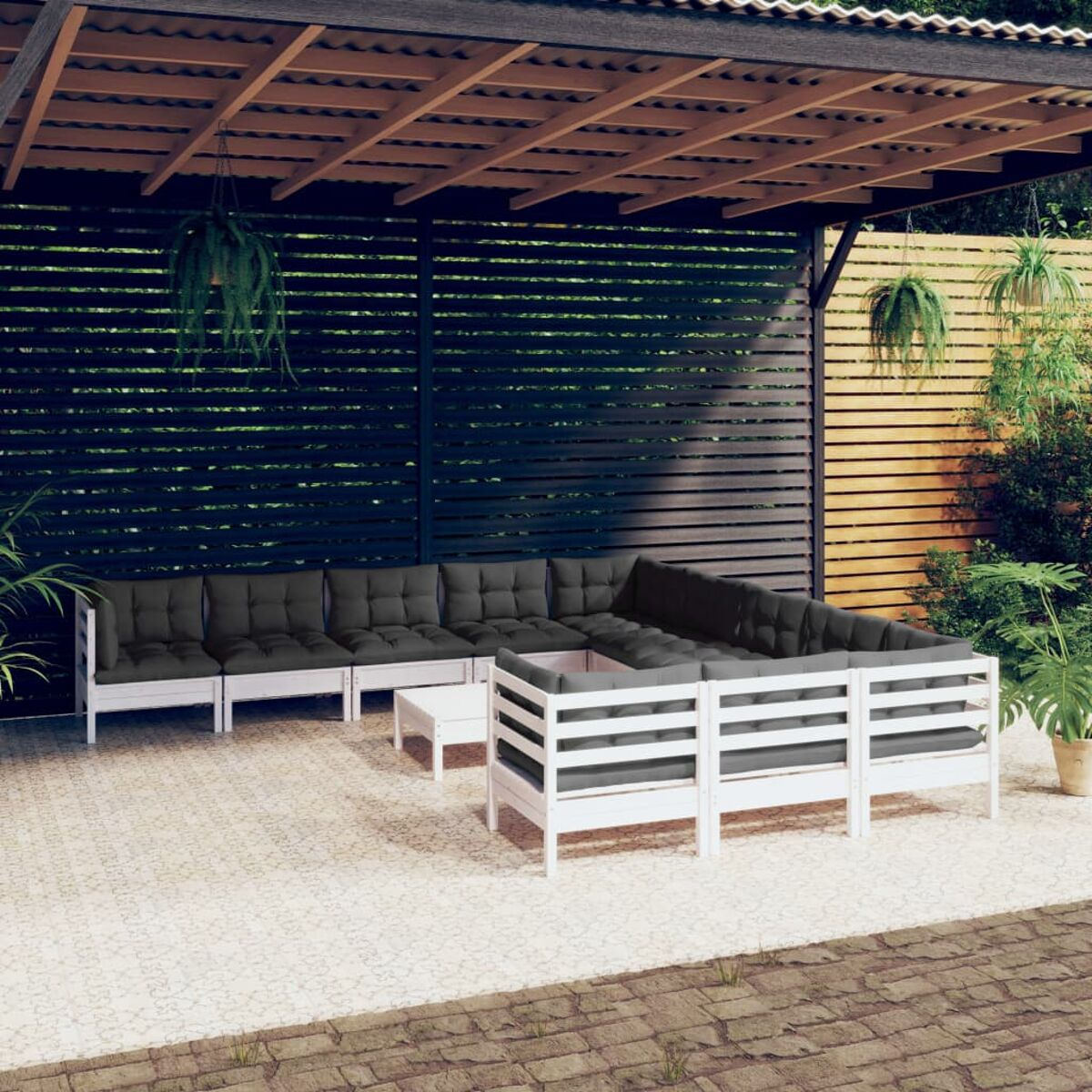 Eine Sitzgruppe im Freien mit weißen Rahmen, schwarzen Kissen und einer Holzpergola.