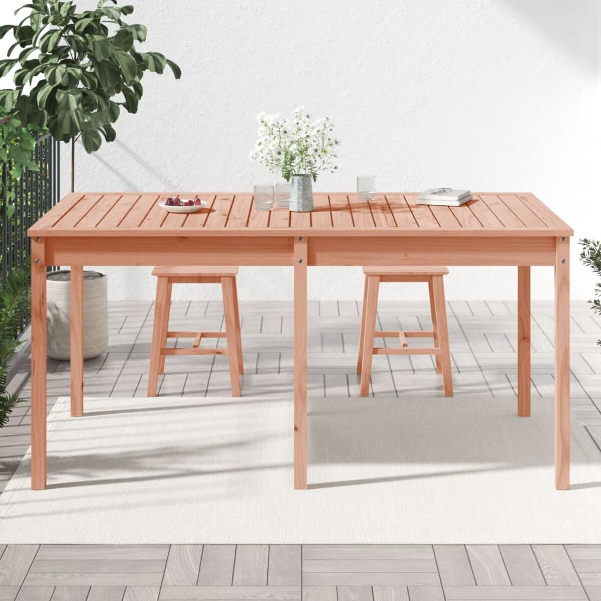 Holztisch im Freien mit zwei Hockern, einer Vase mit Blumen und weiteren Gegenständen.
