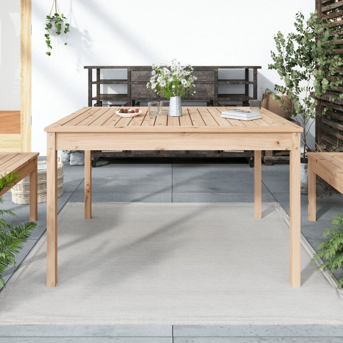 Holz-Esstisch im Freien mit weißem Teppich, Pflanzen und Vase mit Blumen.