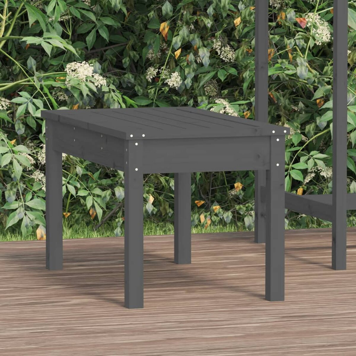 Ein grauer Holztisch mit wenigen sichtbaren Schrauben und einem unscharfen Hintergrund aus Pflanzen.