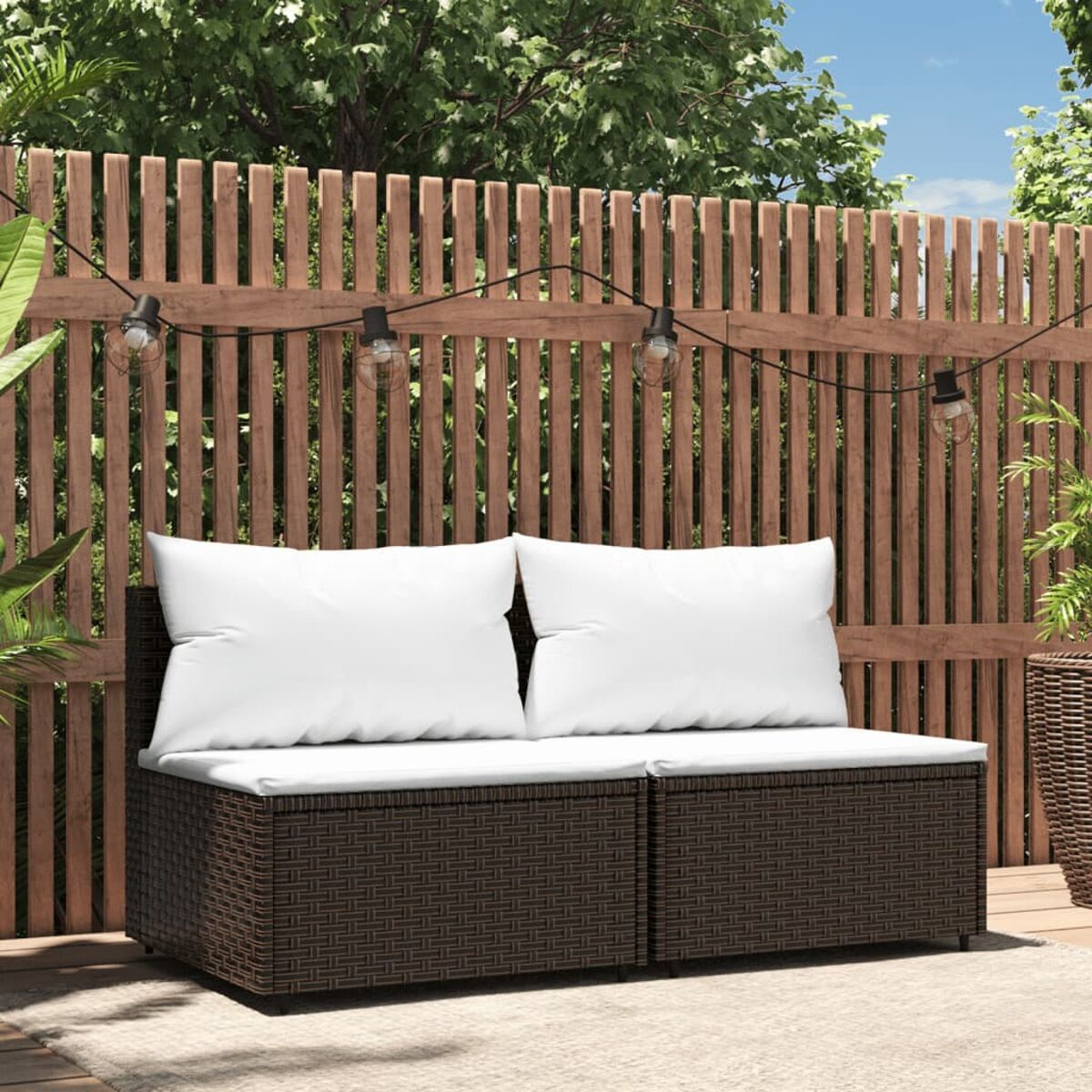 Outdoor-Sofa mit weißen Kissen und braunem Korbboden. Das Sofa steht in einem Garten.