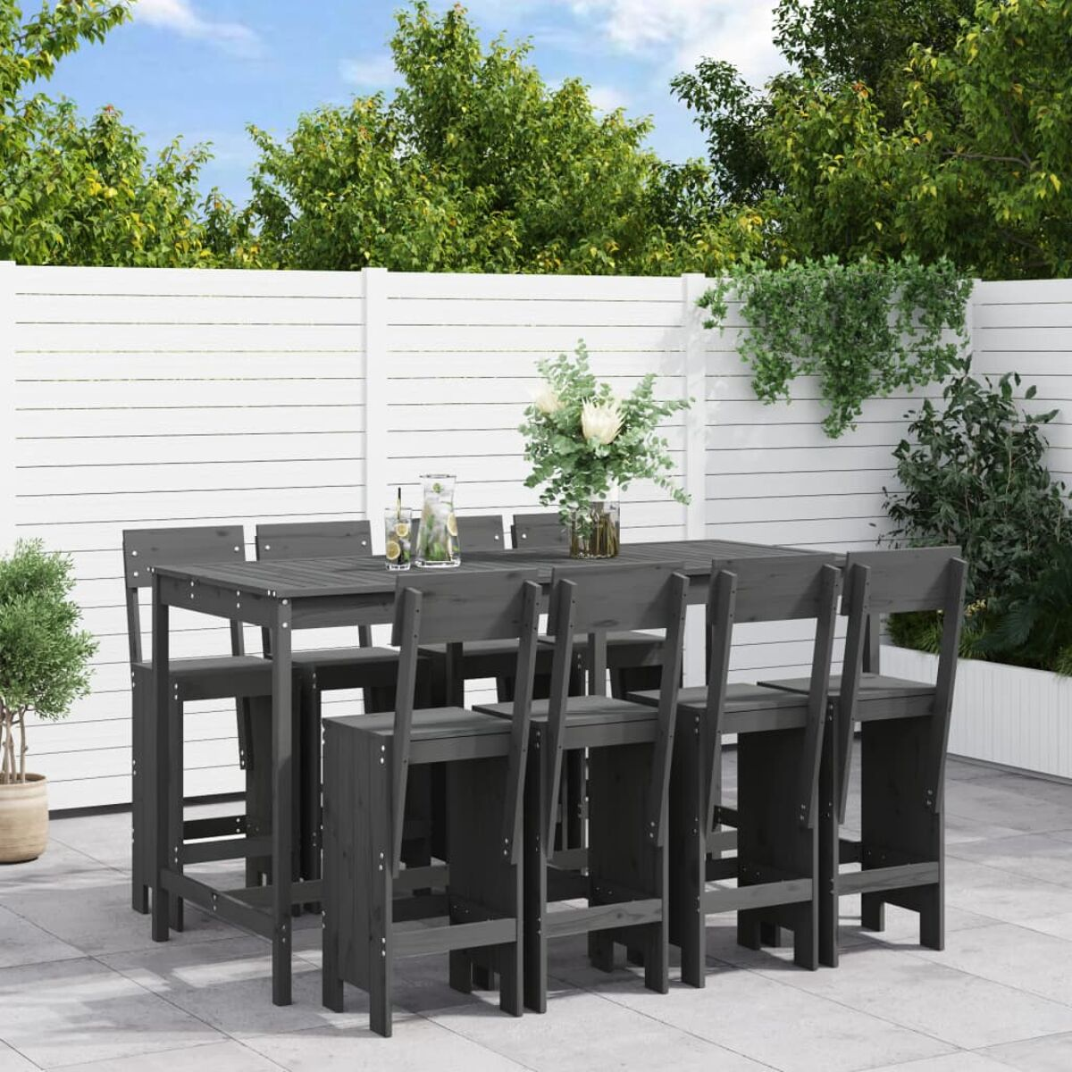 Holzbartisch mit acht Barhockern auf einer Terrasse. Grüne Bäume im Hintergrund.
