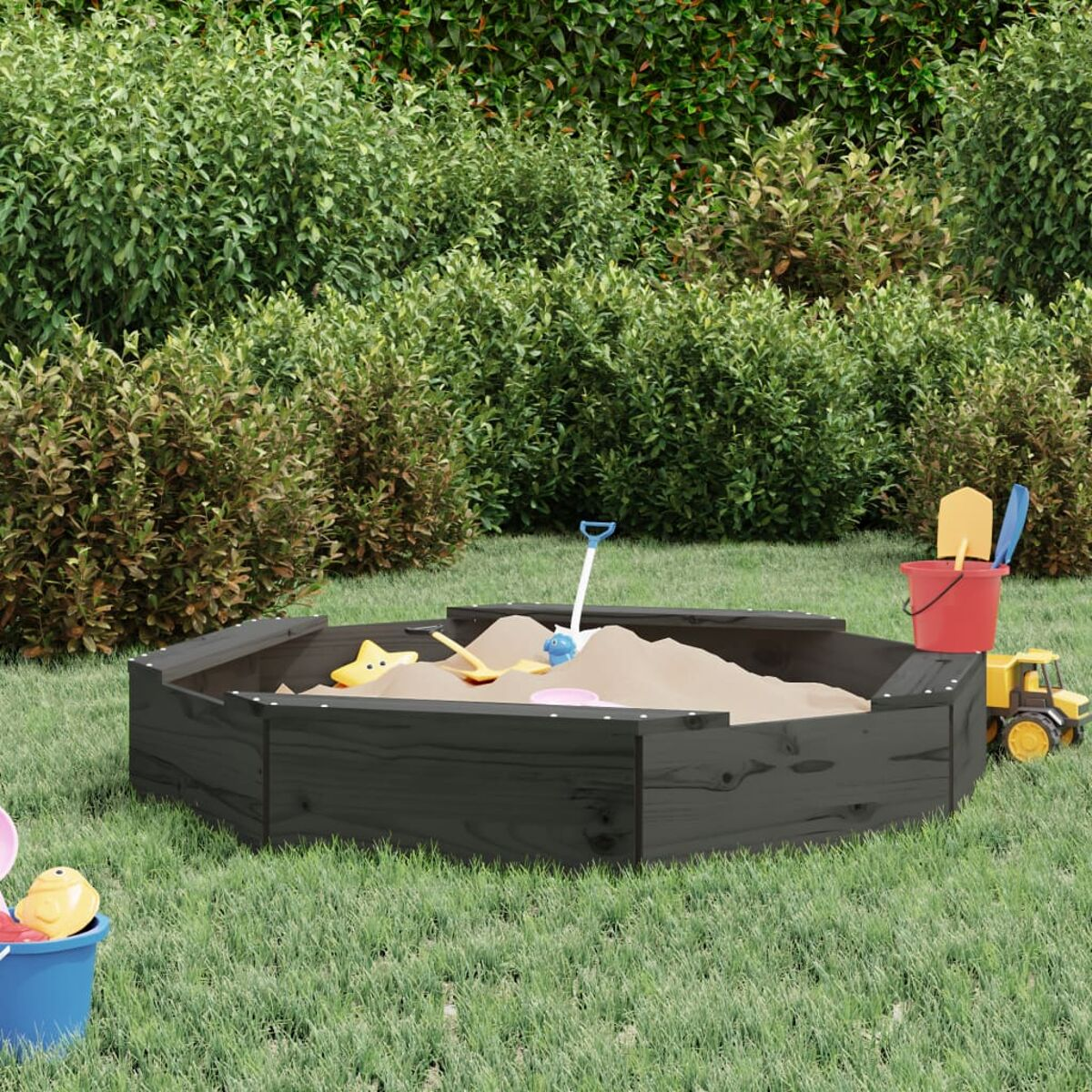 Eine schwarze Sandkiste mit Sand gefüllt. Spielzeuge sind darum herum verstreut.