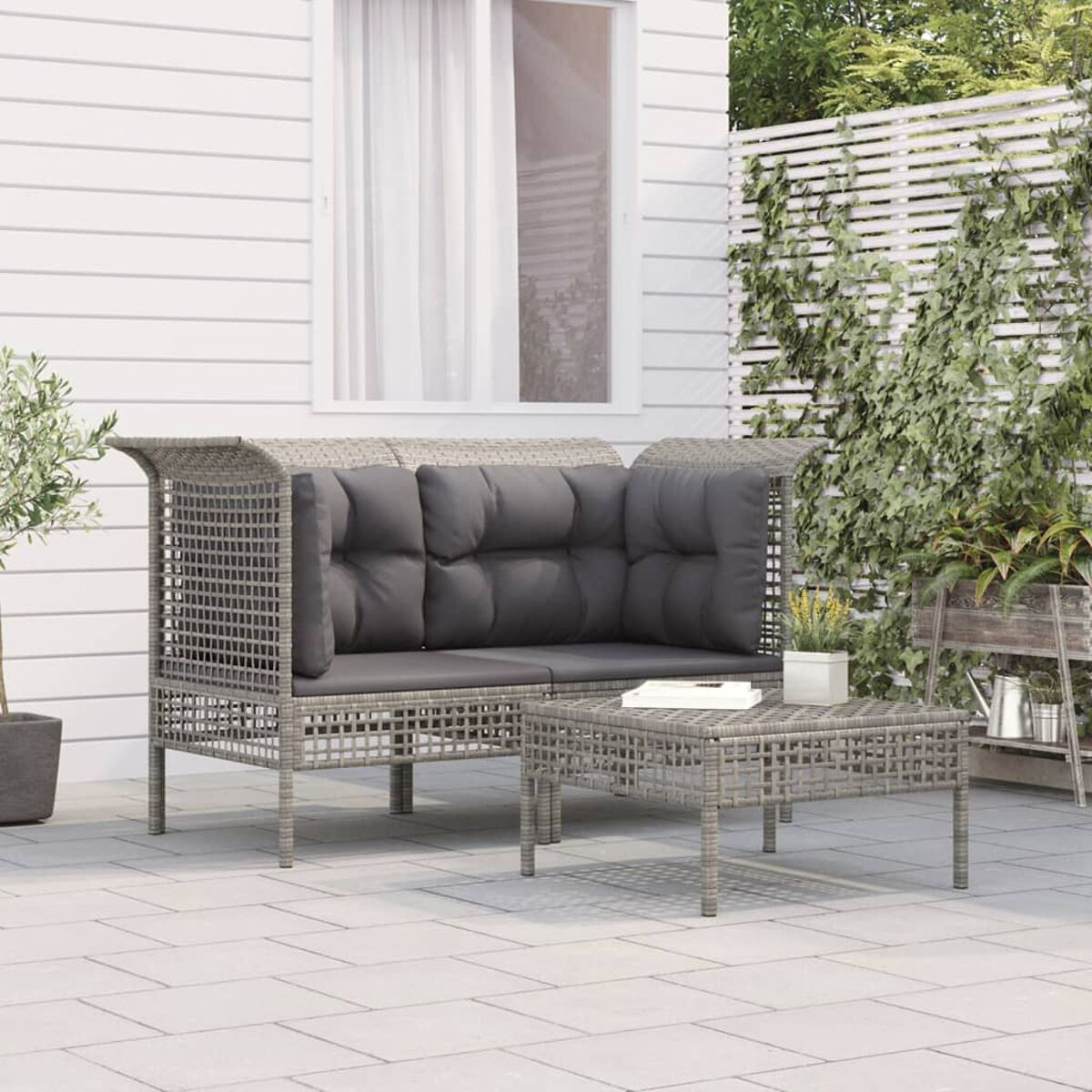 Graues Korbmöbel-Set auf einer Terrasse mit Pflanzen im Hintergrund.