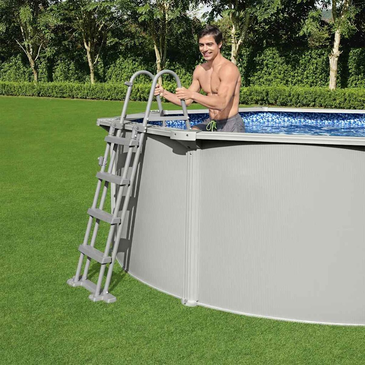 Ein Mann steigt mit einer Leiter aus einem Pool. Grünes Gras und Bäume im Hintergrund.