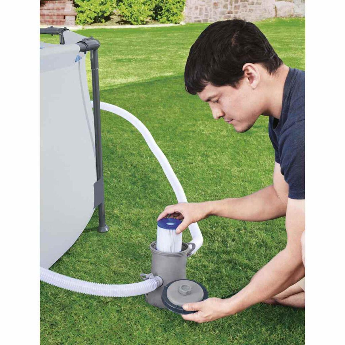 Mann in der Nähe eines Poolfiltersystems. Er hält eine Filterkomponente und befindet sich auf einer Wiese.