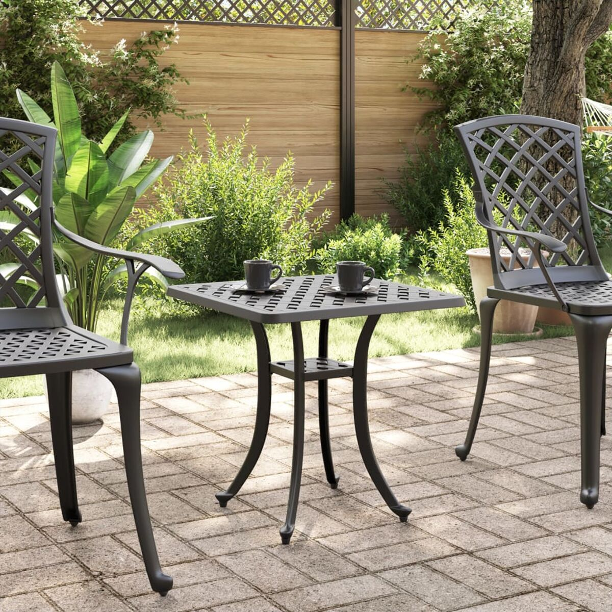 Tisch im Freien mit Stühlen. Schwarzes Metall. Zwei Tassen. Gepflasterte Terrasse.