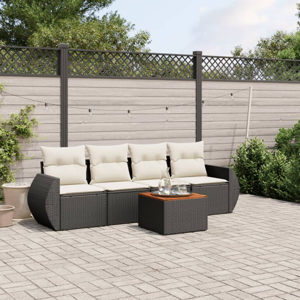 Schwarzes Korbmöbel-Sofa mit cremefarbenen Kissen, Holztisch, Pflanzen im Hintergrund.