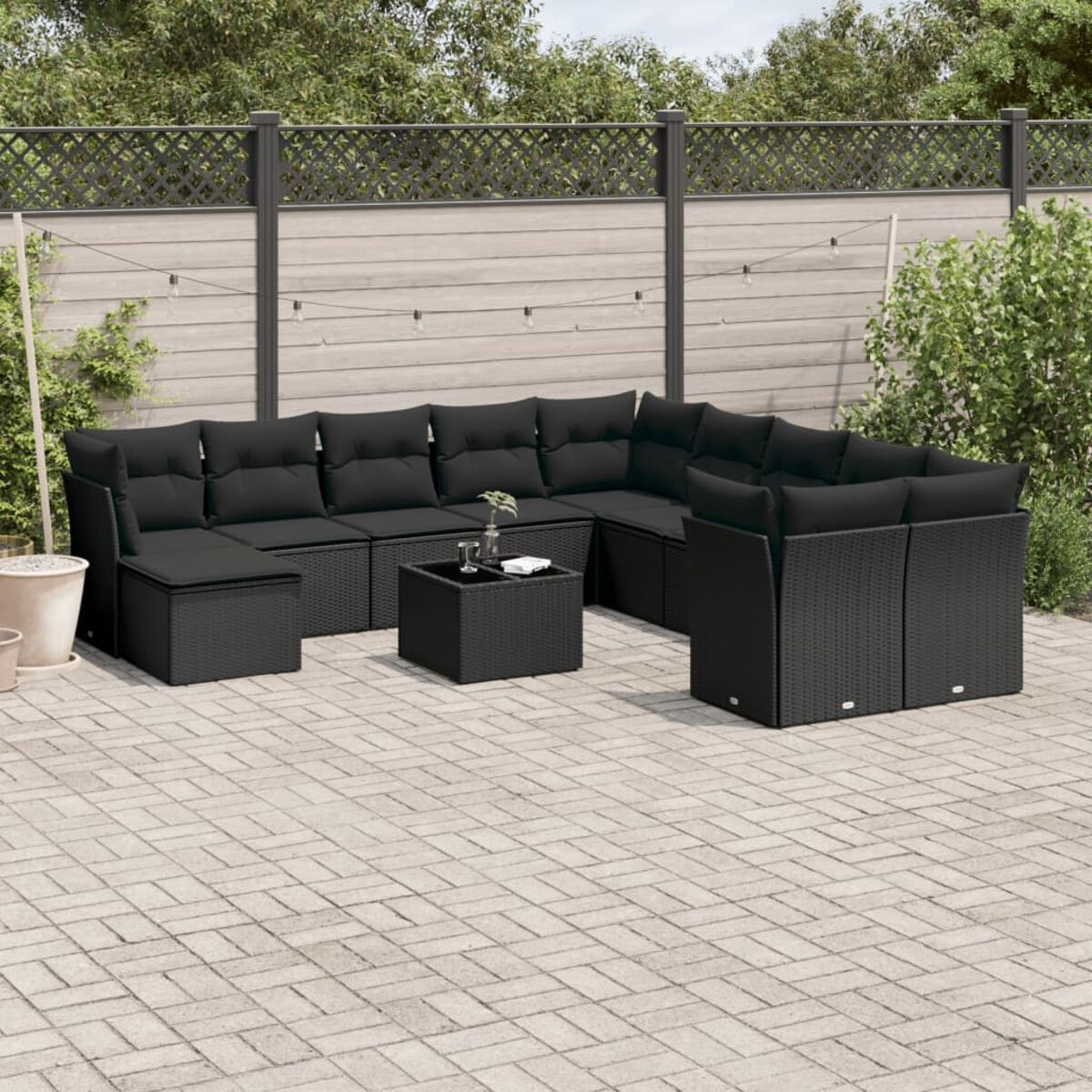 Outdoor-Sitzgruppe mit schwarzen Kissen und einem Couchtisch. Hintergrund: Backstein-Patio, Bäume, Zaun.