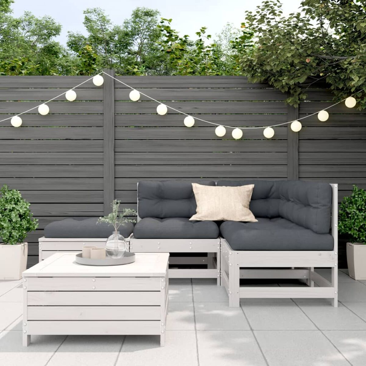Garten-Terrassenset mit weißem Holzrahmen, grauen Kissen, Couchtisch und Lichterketten am Holzzaun.