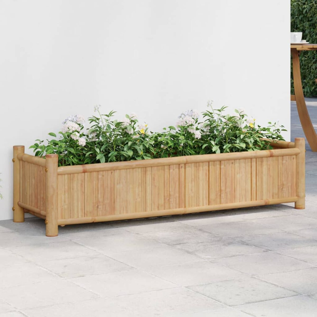 Pflanzkasten aus Holz mit Pflanzen, auf einer Terrasse mit weißer Wand im Hintergrund.
