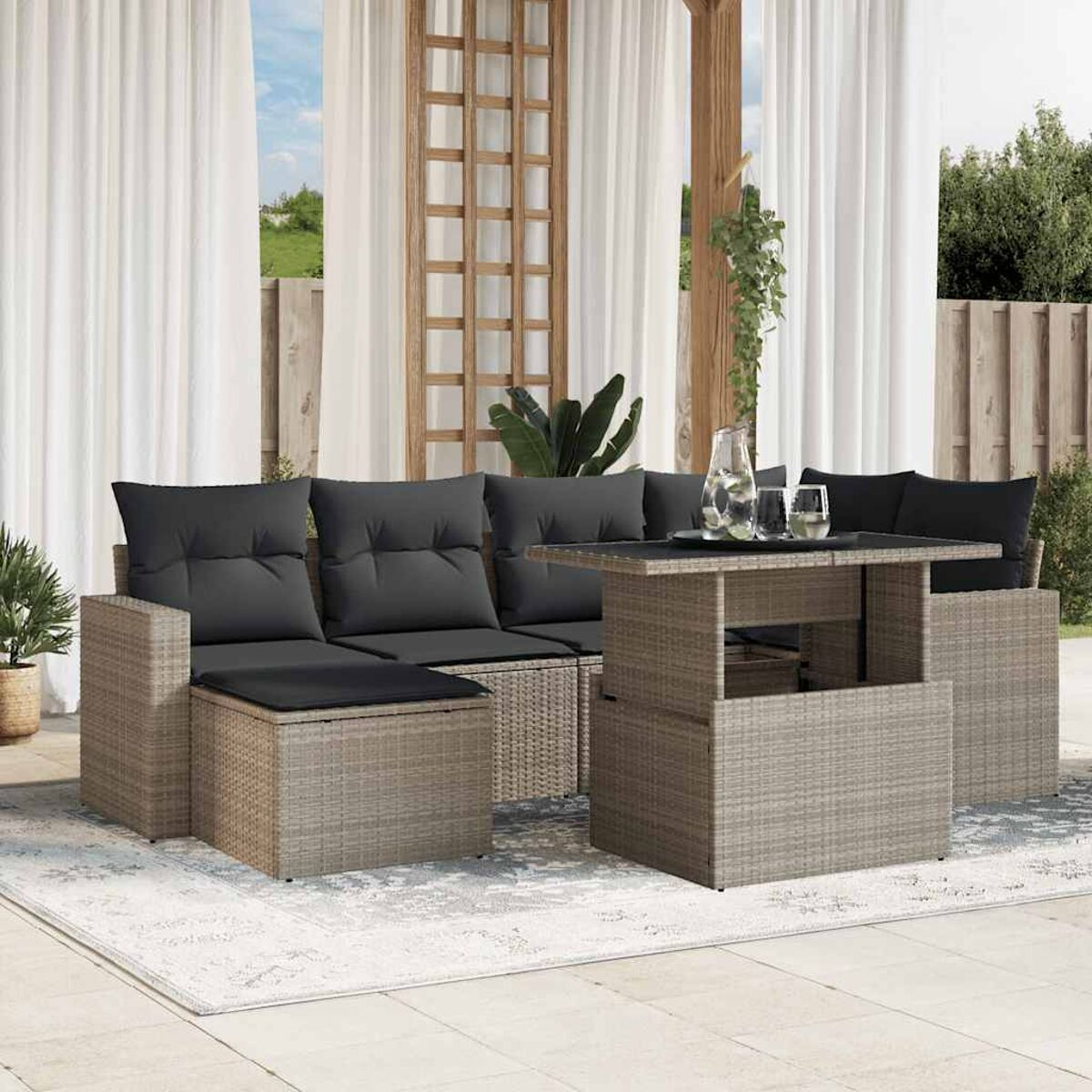 Outdoor-Rattan-Sofagarnitur mit schwarzen Kissen auf einem gemusterten Teppich, mit Tisch und Getränken.
