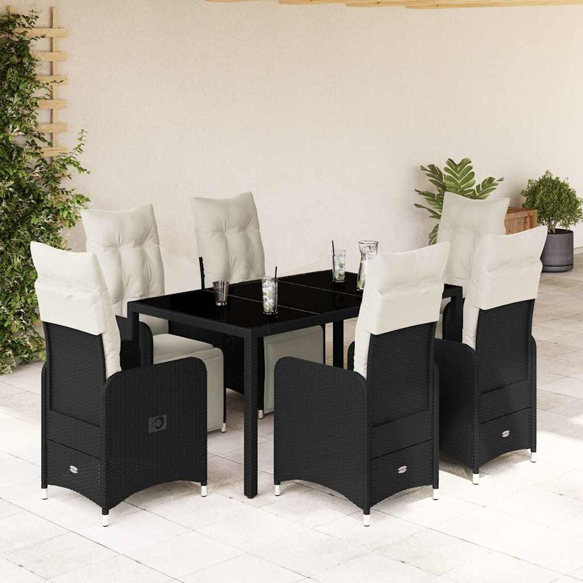 Set da pranzo da esterno in vimini nero con tavolo in vetro e cuscini bianchi. Sfondo muro esterno.