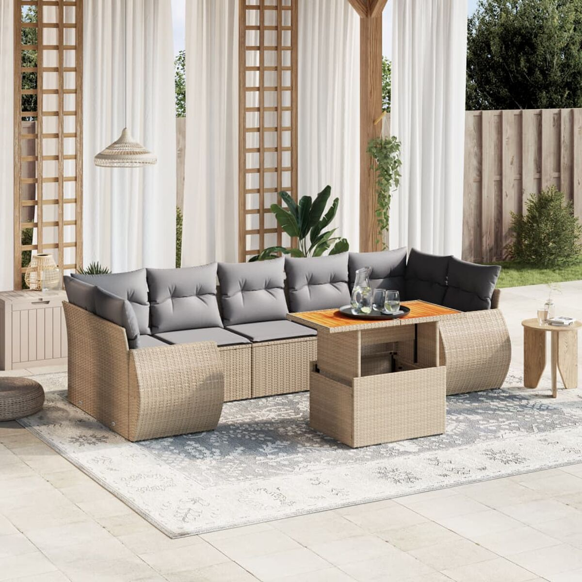 Outdoor-Sitzgruppe mit beigem Korbmöbelsofa, passendem Tisch und grauen Kissen. Vorhänge und Laub im Hintergrund.