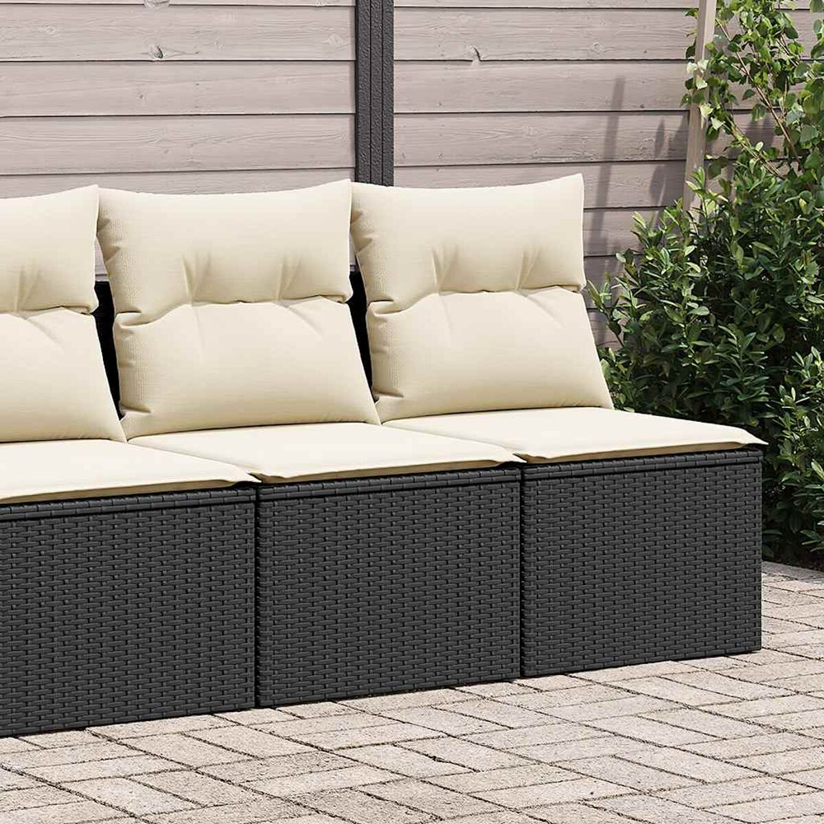 Nahaufnahme eines schwarzen Korbmöbelsofas mit cremefarbenen Kissen auf einer Ziegelterrasse.