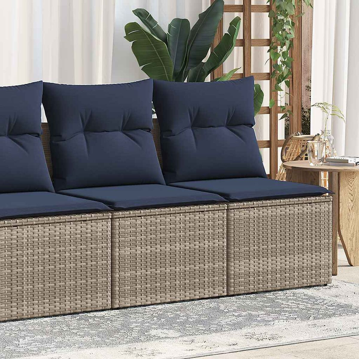 Outdoor-Rattan-Sofagarnitur mit blauen Kissen. Das Sofa steht auf einem hellgrauen Teppich.