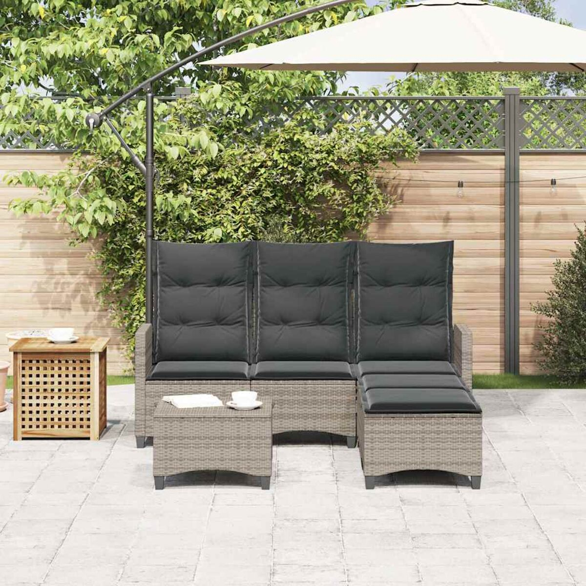 Set divano esterno in rattan grigio con cuscini, pouf e ombrellone sullo sfondo.