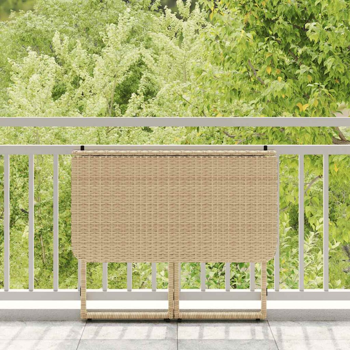 Una mesa plegable de mimbre beige en un balcón con barandilla blanca y vegetación al fondo.