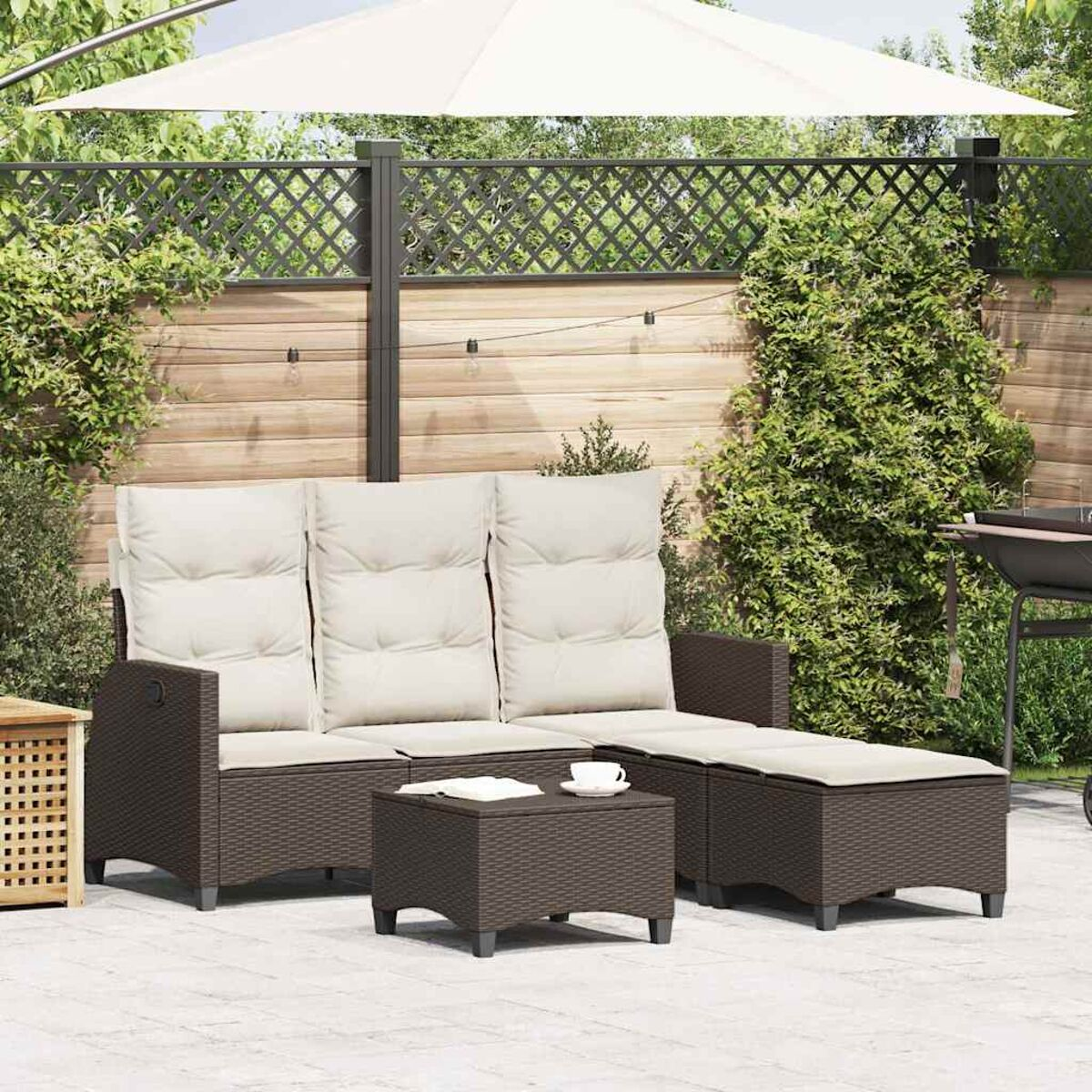 Set di mobili da esterno in rattan marrone: divano, pouf e tavolino. Erba verde e recinzione.