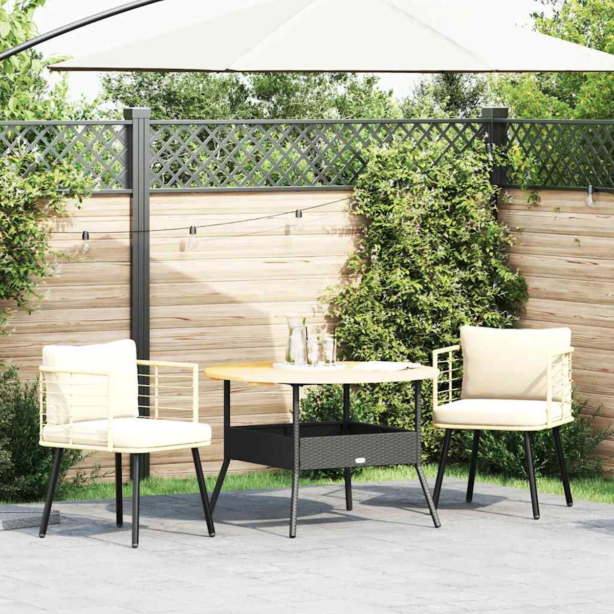 Terrassenset: zwei Stühle, runder Tisch und Sonnenschirm. Holzzaun im Hintergrund. Grünes Laub.